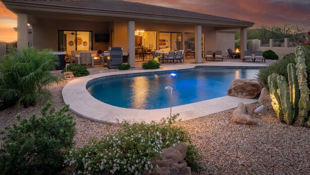 Ein modernes Haus mit Swimmingpool, Terrassenmöbeln und einem Garten in Wüstentypologie.