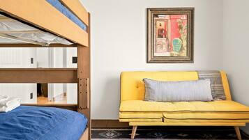 A bunk bed with a blue blanket, a yellow sofa with a gray pillow, and a framed picture on the wall.