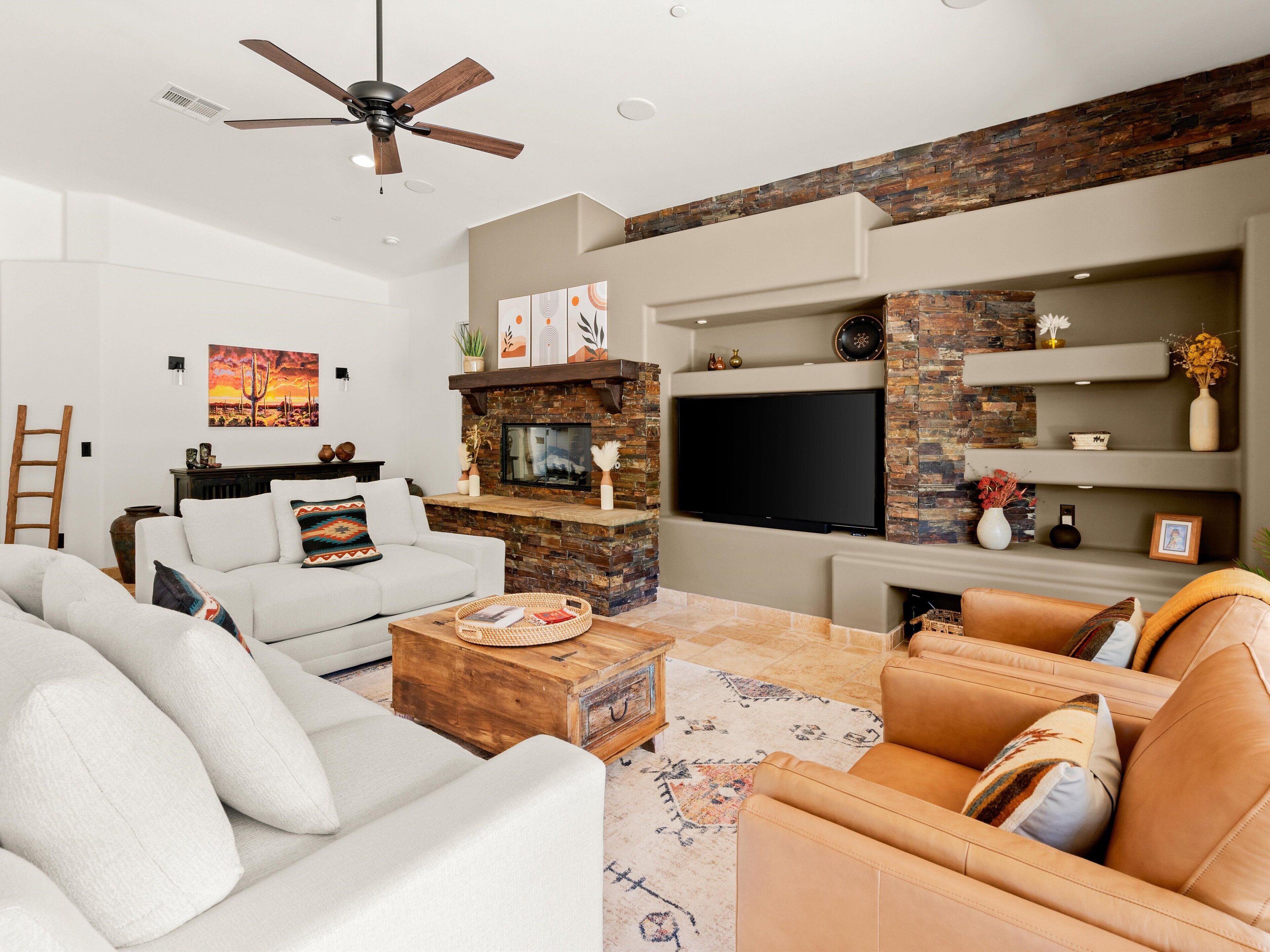 A modern living room with a fireplace, a flat-screen TV, and a ceiling fan.