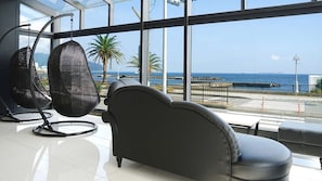 Een moderne kamer met een groot raam, een zwarte leren bank en een rieten stoel.