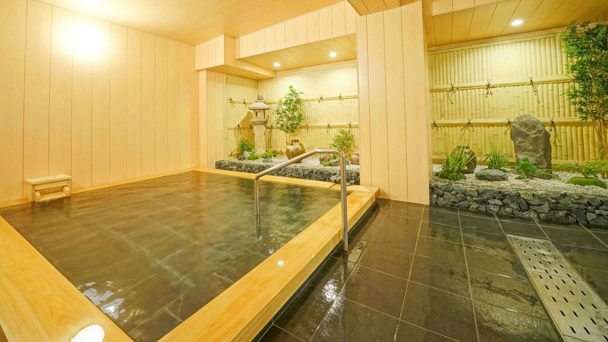 A hot spring bath with a wooden bench, stone wall, and bamboo decorations.