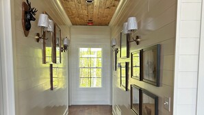 A hallway with wooden floors and walls, featuring framed pictures and wall-mounted lights.