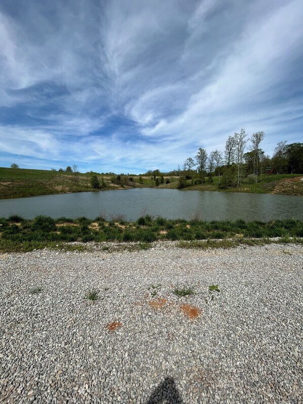 A gravel path leading to a calm lake surrounded by trees and grassy areas. - Luxury in the Country. Chalet Style Cabin on secluded 61 Acres with 3 acre Lake (Bloomfield)