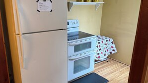 Une cuisine compacte équipée d’un réfrigérateur, d’un four et d’un four à micro-ondes. Le sol est en bois et il y a une petite étagère avec des bocaux.