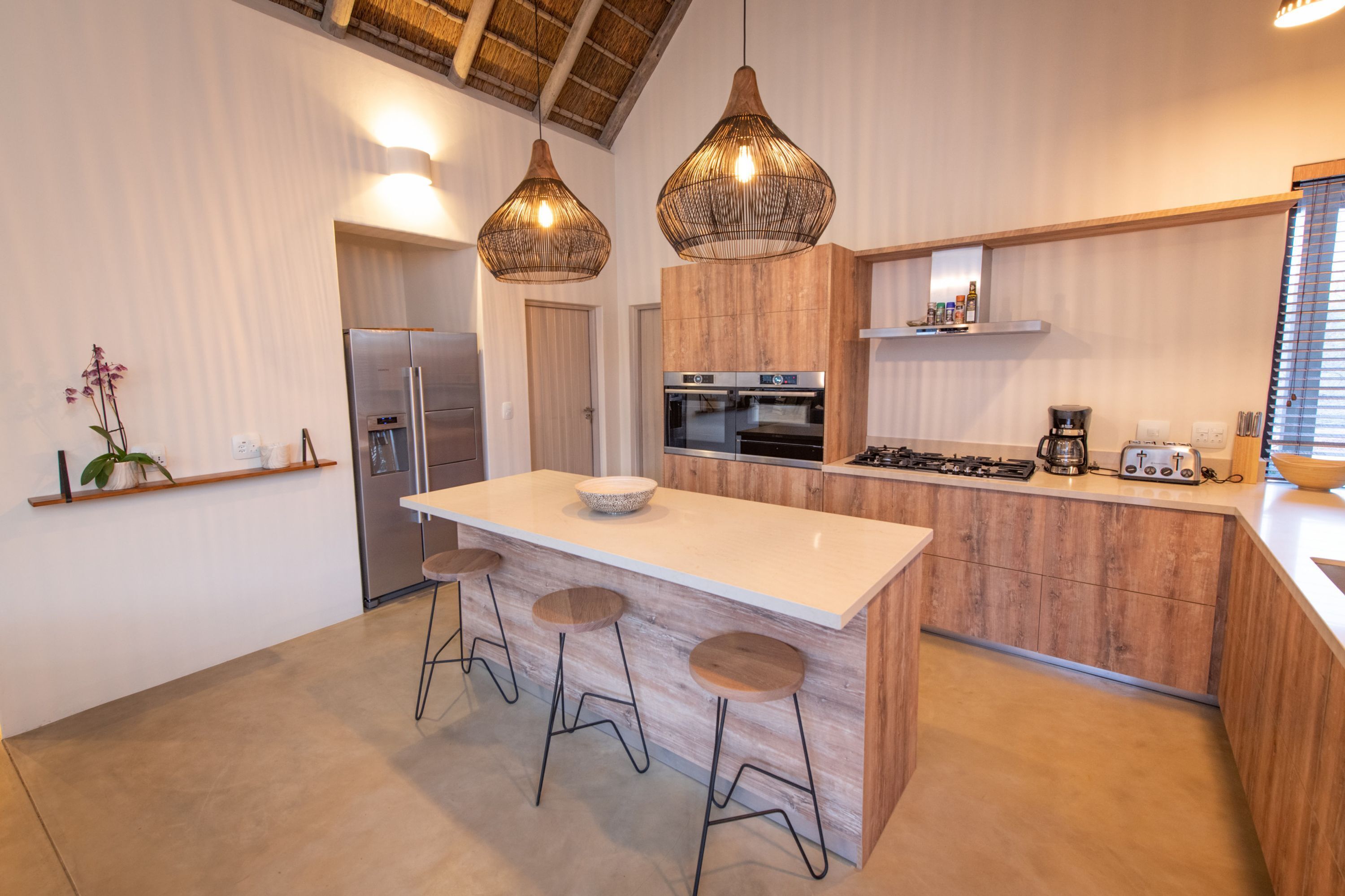 A modern kitchen with a central island, bar stools, a refrigerator, an oven, a stove, and hanging pendant lights.