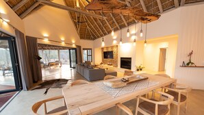 A spacious living area with a large wooden dining table, comfortable seating, a stone fireplace, and a TV mounted on the wall. - Villa Appelblaar in Hoedspruit (Hoedspruit)