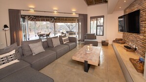 A modern living room with a sectional sofa, a coffee table, a flat-screen TV, and a stone accent wall. - Villa Appelblaar in Hoedspruit (Hoedspruit)