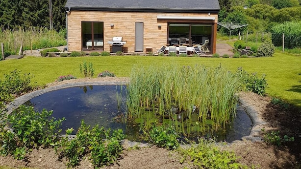 Une maison moderne dotée d’un grand garage, d’une piscine et d’un jardin avec un étang.