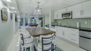 Een moderne keuken met witte kasten, een magnetron en een eethoek met een pooltafel.