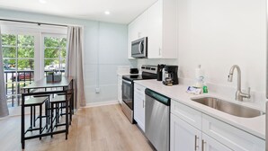 Une cuisine moderne avec des meubles blancs, des appareils en acier inoxydable et une grande fenêtre donnant sur un parking.