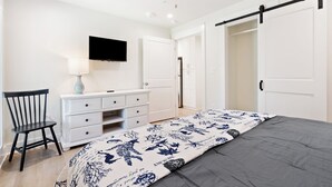 Une chambre à coucher comprenant un lit, une commode, une chaise, un téléviseur fixé au mur et un placard à portes coulissantes.