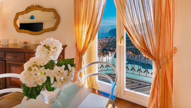 A room with a dining table, white flowers, a mirror, and a view of a pool and cityscape through a door.