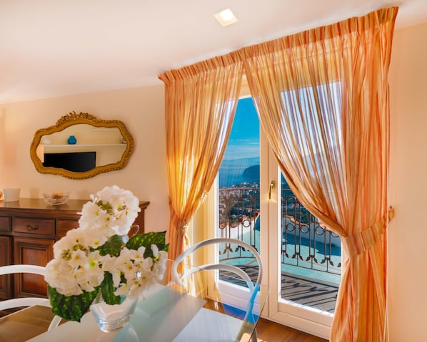 Une piĂšce comprenant une table Ă manger, des fleurs blanches, un miroir et une vue sur une piscine et le paysage urbain, visible Ă travers une porte.