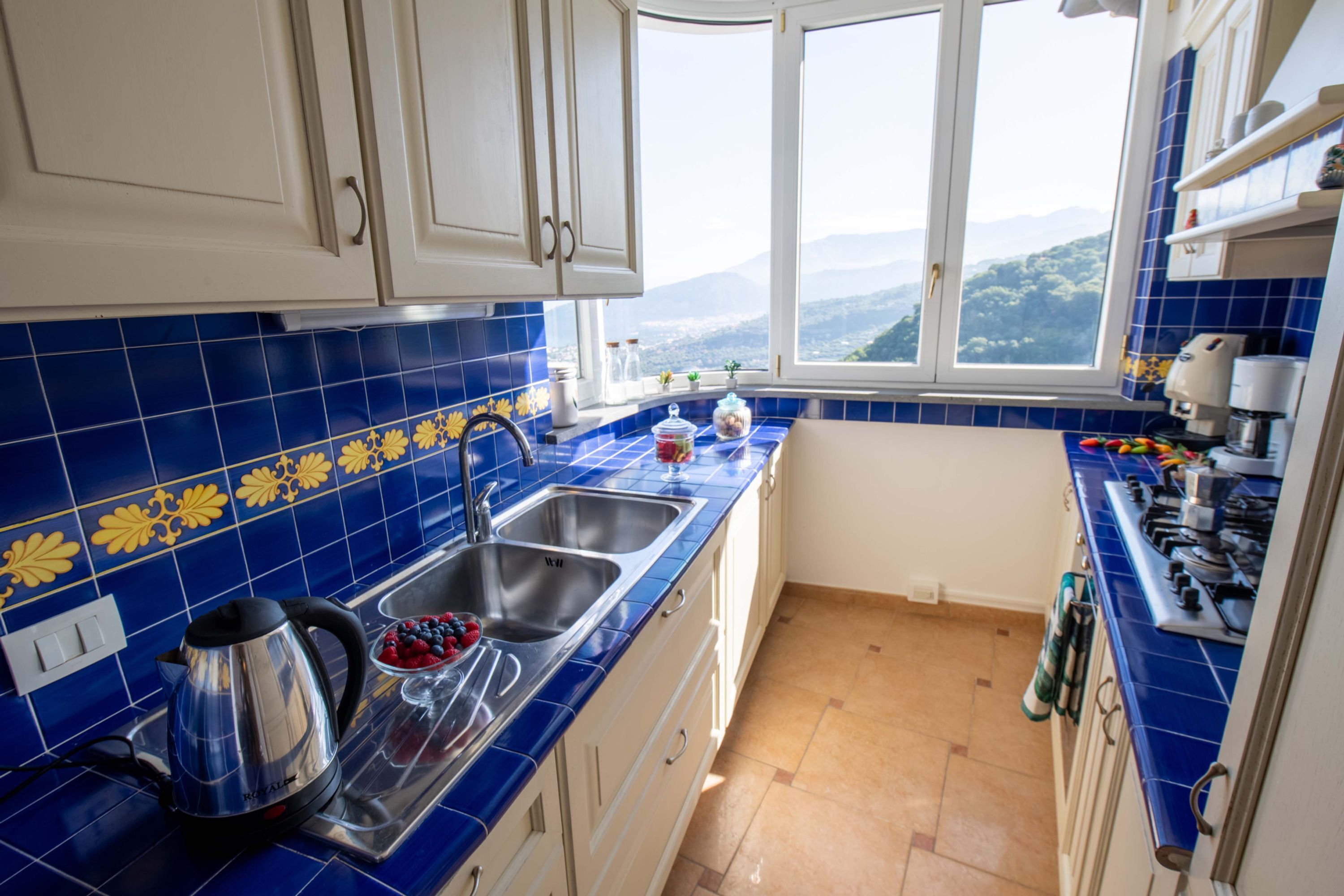 Een keuken met blauwe tegels, roestvrijstalen apparatuur en een raam met uitzicht.