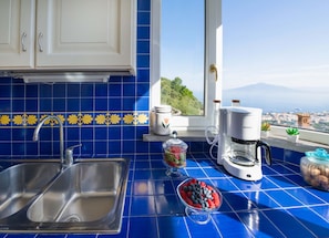 A kitchen with a sink, a coffee maker, and a window with a view of a city and mountains. - Villa Grazielluccia in Sorrento (Sorrento)