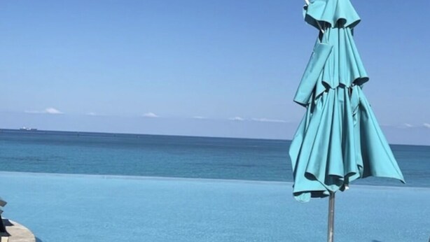 Una piscina azul cristalina con una sombrilla turquesa y sillones de descanso.