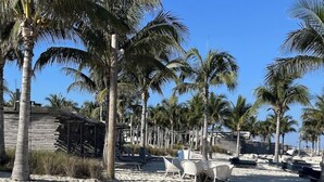 Una playa con palmeras, sillas de descanso blancas y una estructura de madera.