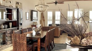 Un comedor espacioso con una gran mesa de madera, sillas de mimbre, una lámpara de araña y un ventilador de techo.