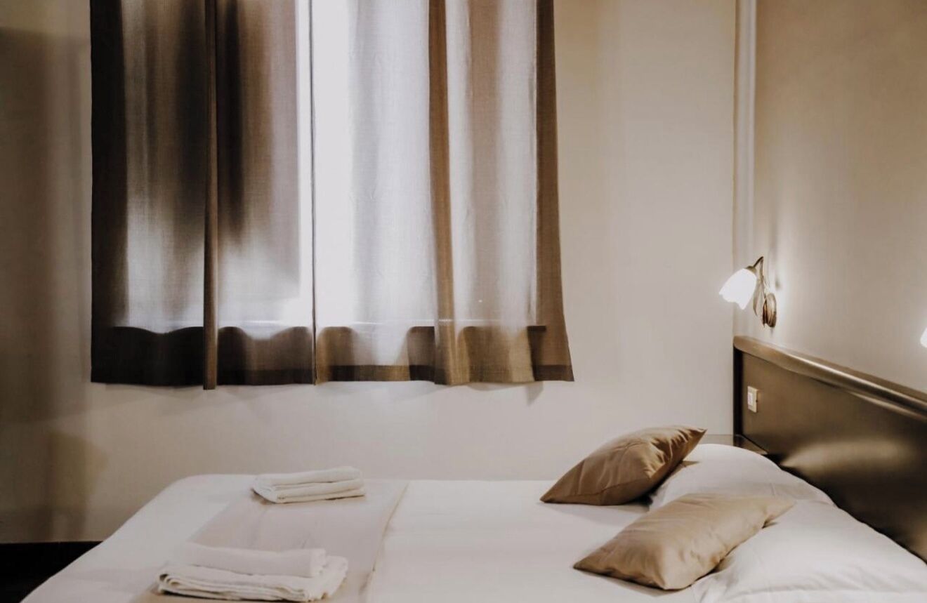 A hotel room with a neatly made bed, a bedside lamp, and curtains.