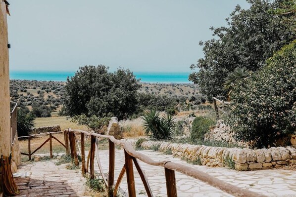 A stone pathway leading to a scenic overlook with views of the sea and surrounding vegetation. - Agriturismo Balcone Mediterraneo Camere (Ragusa)