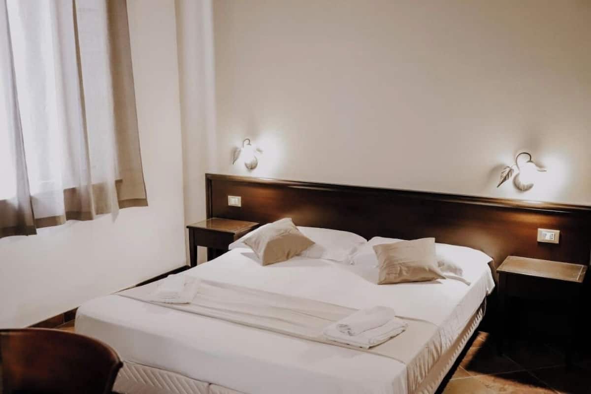A hotel room with a neatly made bed, two bedside tables, and a chair.