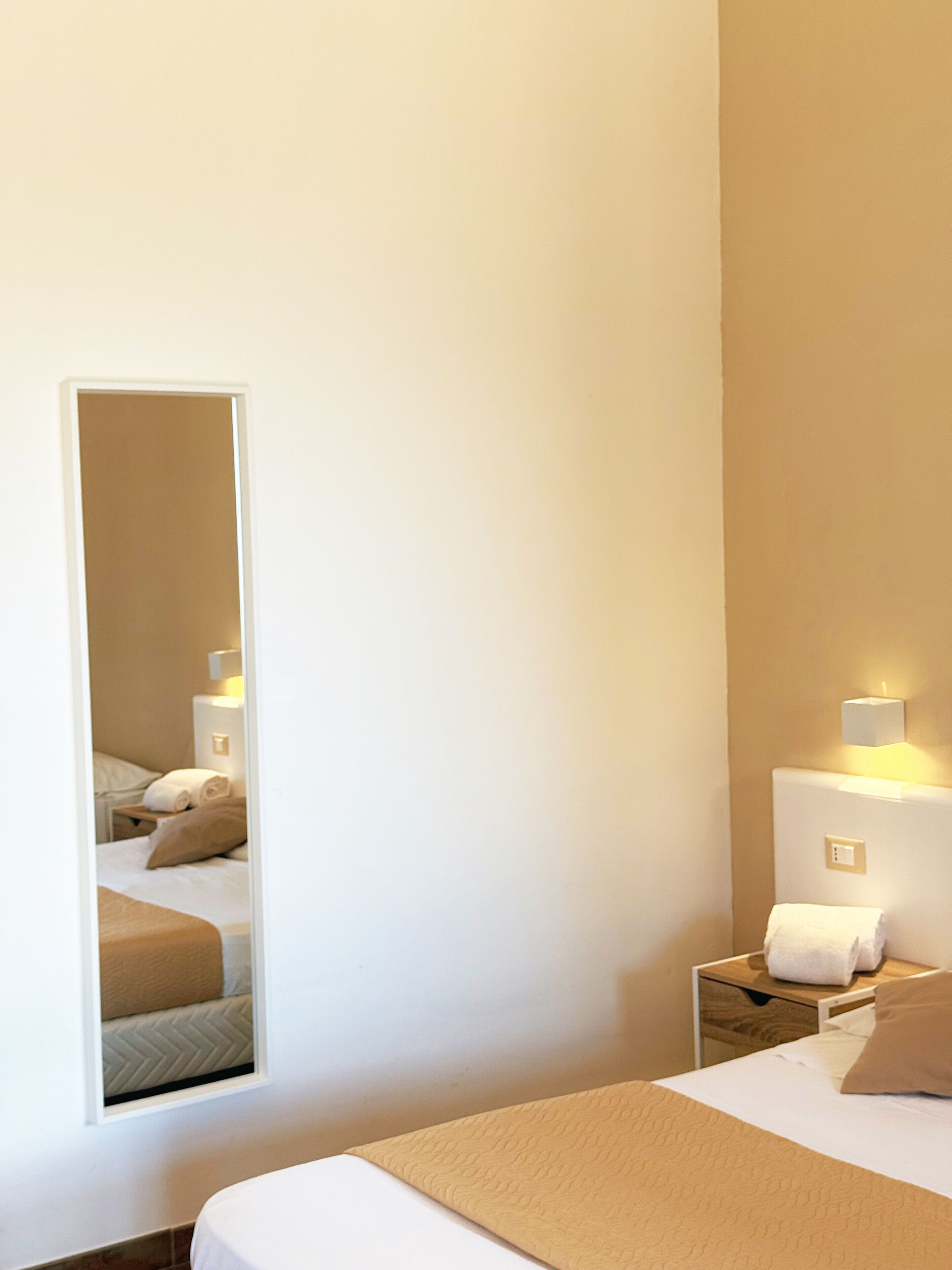 Een hotelkamer met een bed, nachtkastje, spiegel en een wandlamp.