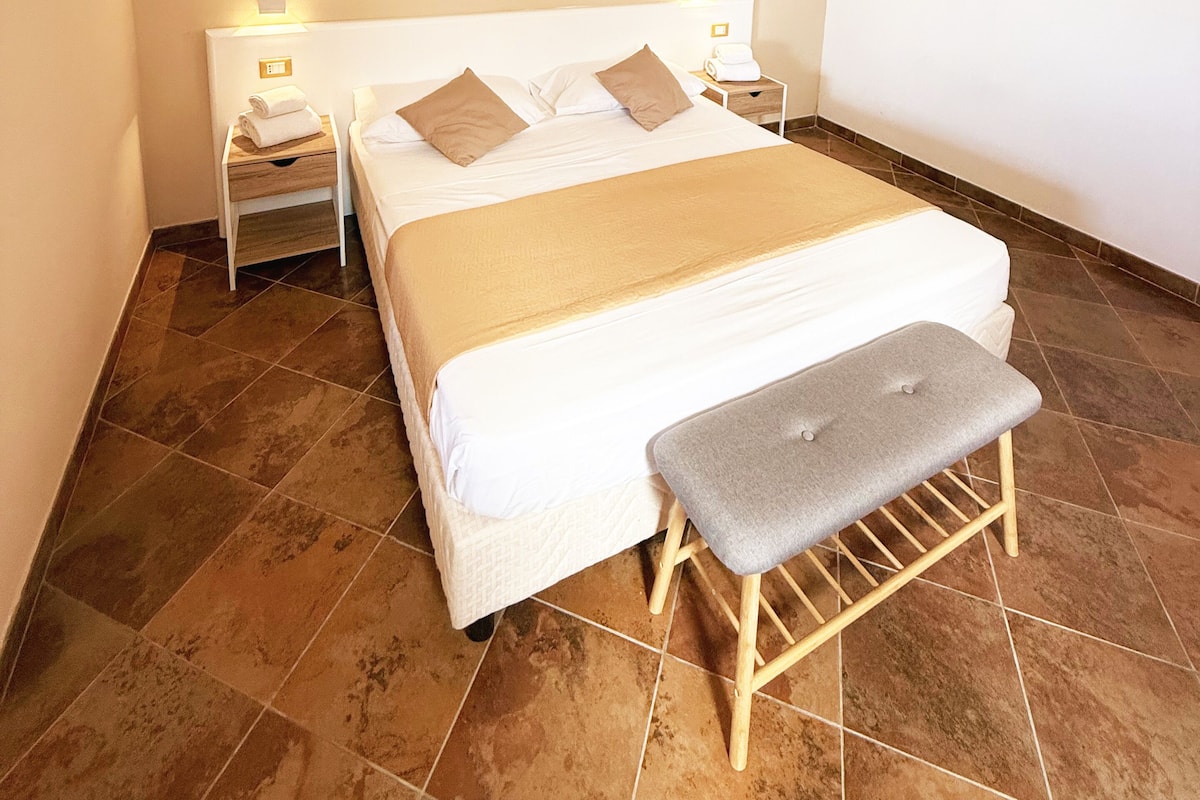 A bedroom with a large bed, two bedside tables, a bench, and a stone accent wall.