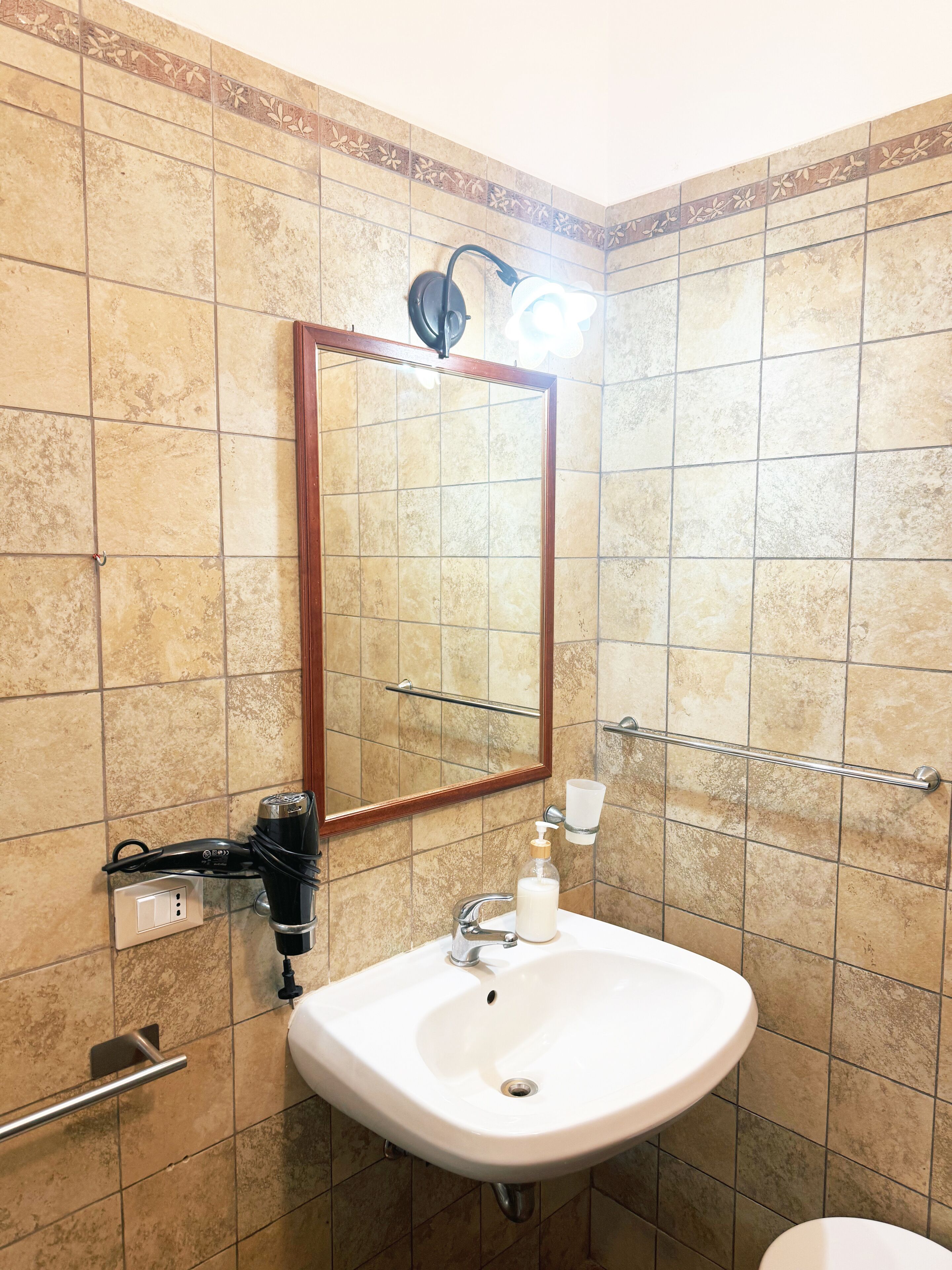 Un baño con un lavamanos blanco, un espejo y un perchero para toallas.