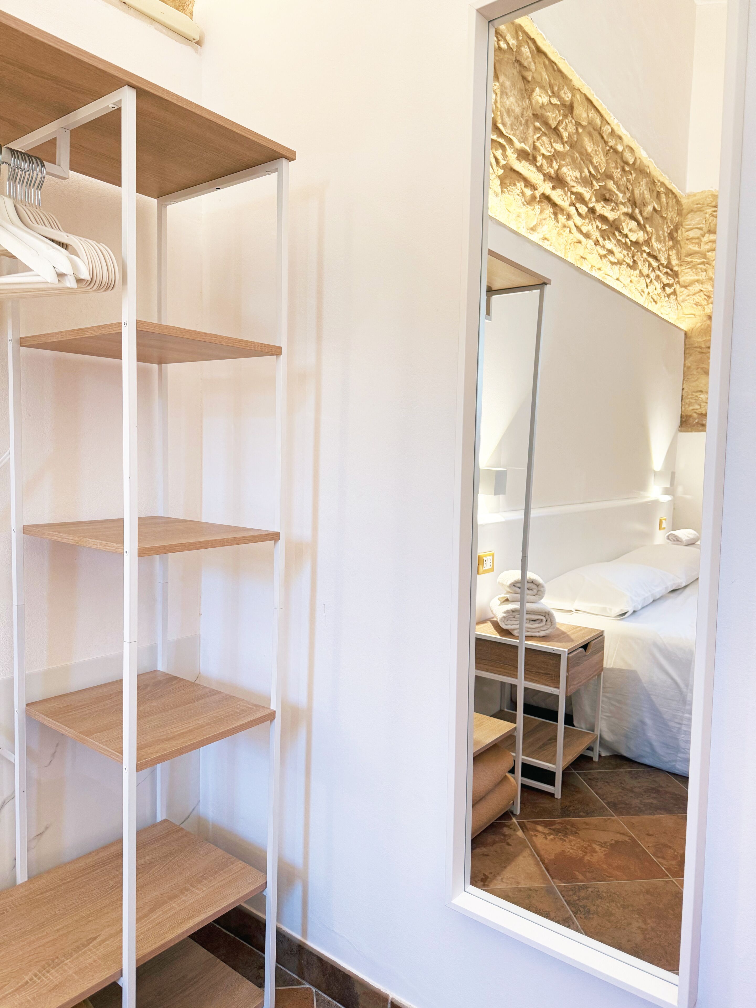 Une chambre d’hôtel avec une armoire à miroir, un lit avec du linge de maison blanc et une petite table de chevet avec une lampe.