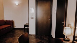 A hotel room with a dark wooden door, a small table with a lamp, a red sofa, and a chair. - Agriturismo Balcone Mediterraneo Camere (Ragusa)