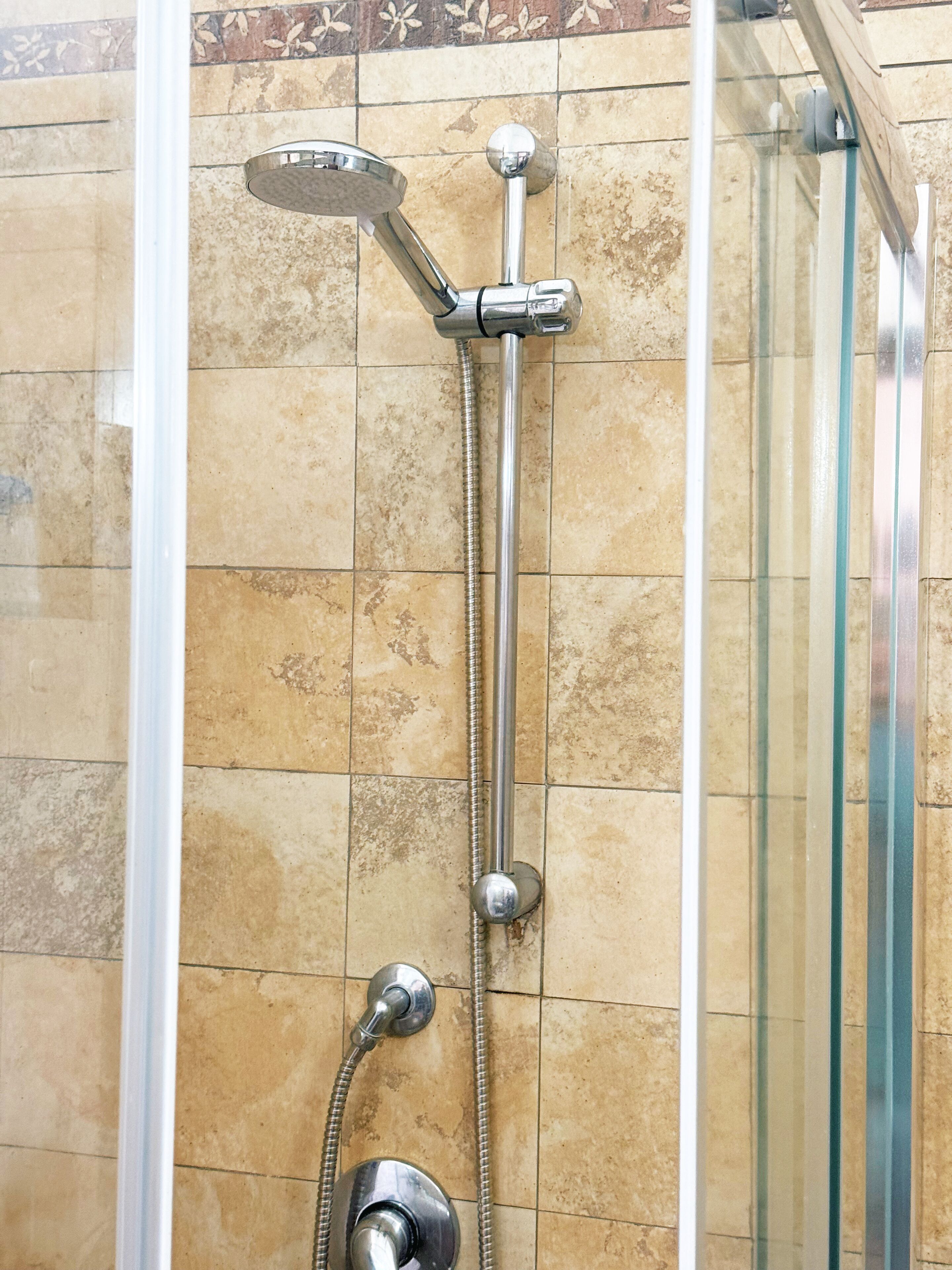 Ducha con cabezal de ducha manual y cabezal fijo, ambos instalados en una pared con un salpicadero de azulejos.