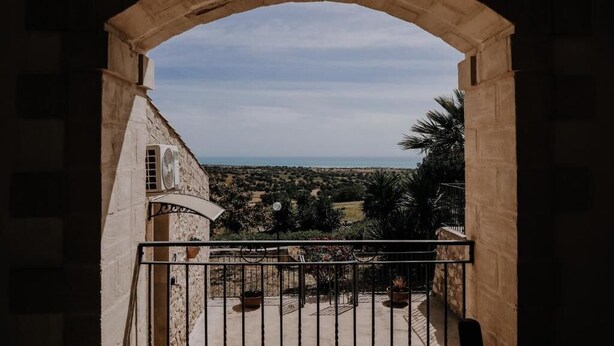 A balcony with a stone archway overlooking a landscape with trees and a distant view. - Agriturismo Balcone Mediterraneo Camere (Ragusa)