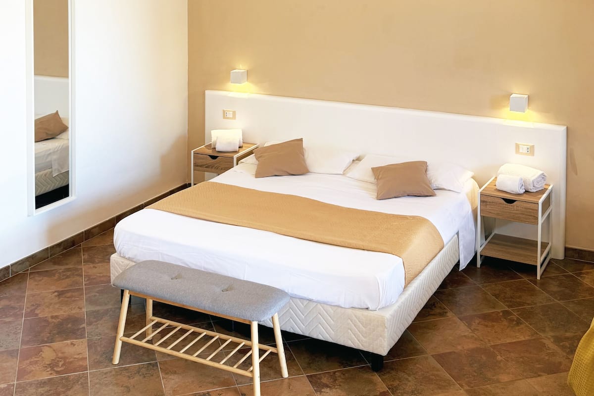 A bedroom with a large bed, two bedside tables with lamps, a bench, and a mirror.
