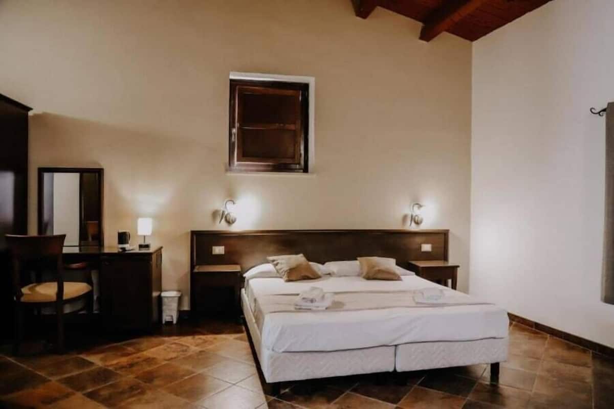 A bedroom with a large bed, two bedside tables, a chair, a desk, and a mirror.