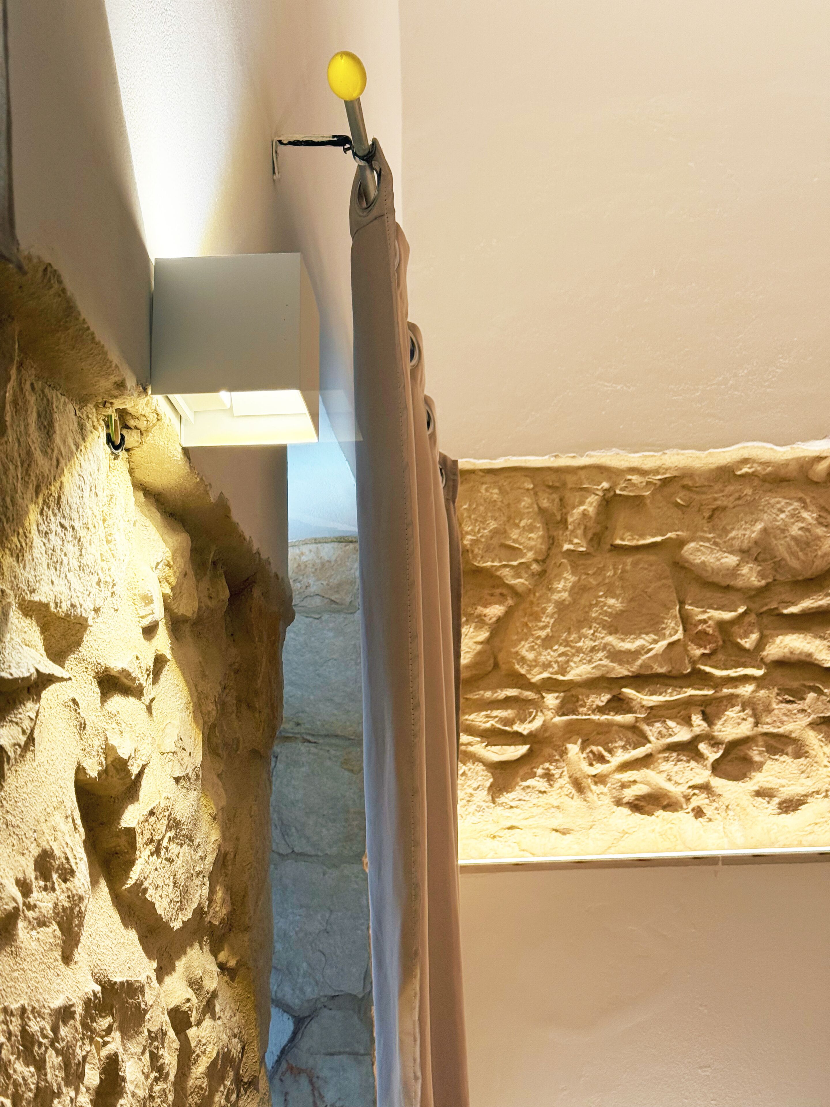 Un baño con pared de piedra, cortina de ducha y un perchero con un pomo amarillo.