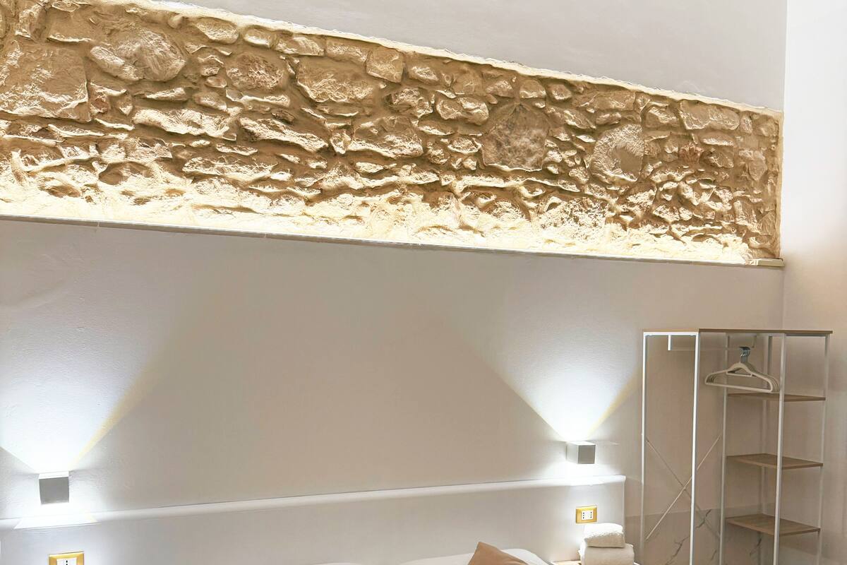 A neatly arranged hotel room with a large bed, two bedside tables, a wall-mounted shelf, and a wardrobe.