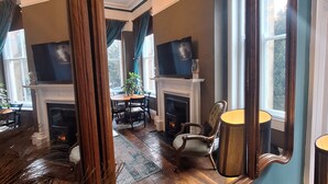 A room with a fireplace, a mirror, and a dining area with chairs and a table. - Huntress Suite, Buxton - a beautiful victorian apartment with private parking. (Buxton)