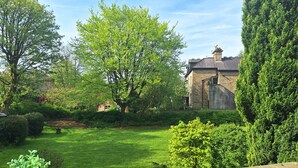 A lush garden with a stone building, a lawn, and a table with chairs. - Huntress Suite, Buxton - a beautiful victorian apartment with private parking. (Buxton)