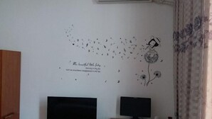 A room with two monitors on a desk, a wall decal with a girl and birds, and a window with curtains. - Quanzhou Longshi Hotel (Quanzhou)