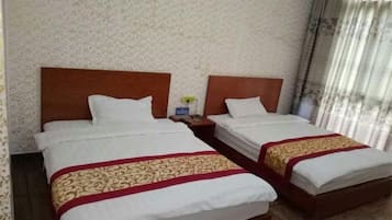 Habitación doble con dos camas, cada una con cabecera de madera, ropa de cama blanca y almohada decorativa roja y dorada.