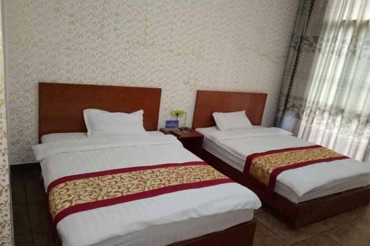Habitación de hotel con dos camas, cada una con ropa blanca y un detalle decorativo rojo y dorado.
