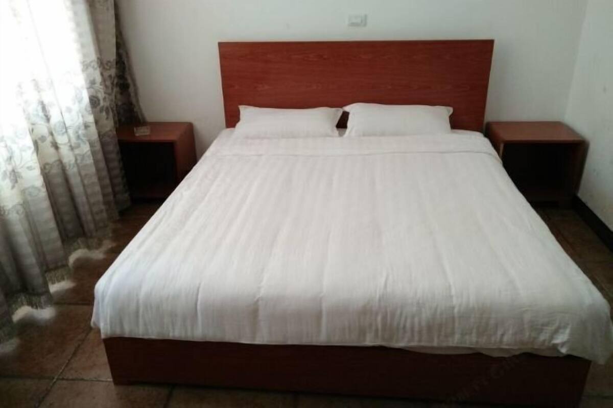 Una habitación de hotel estándar con una cama individual, dos mesitas de noche y una cortina.
