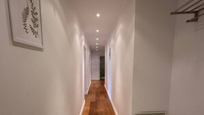 Un estrecho pasillo con suelo de madera y paredes blancas que conduce a una habitación con piso de mármol.