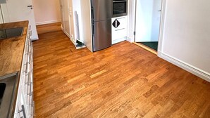 Una cocina moderna con refrigerador, horno y microondas de acero inoxidable. El piso es de madera y las paredes son blancas.