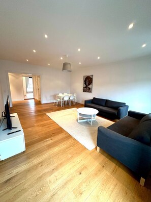 A spacious living area with a dark blue sofa, a white coffee table, and a dining table with chairs. - Luxury Apartment in City (Gothenburg)