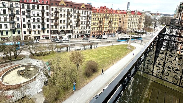 Vista desde un puente sobre una ciudad con edificios de varios pisos, una línea de tranvía y un parque circular.