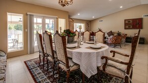Een eetruimte met een ronde tafel voor vier personen, omringd door decoratieve stoelen, een kroonluchter en uitzicht op het buitenlandschap door grote ramen.