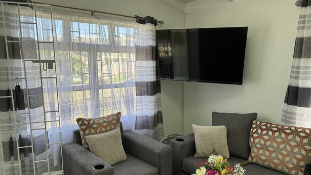 Een woonkamer met grijze banken, gestreepte kussens, een flatscreen-tv en een raam met dunne gordijnen.