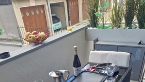 An outdoor dining area with a table set for two, including plates, cutlery, and a bottle of wine.
