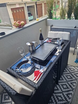 An outdoor dining area with a table set for two, including plates, cutlery, and a bottle of wine.